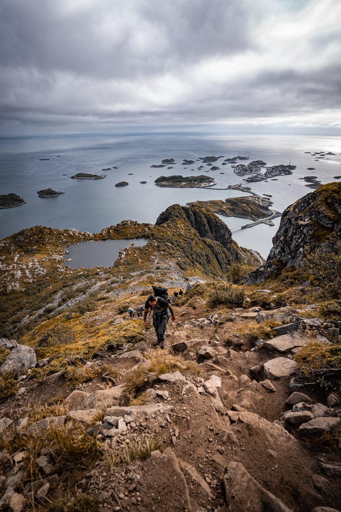 Services Adventurer hiking on rocky trail overlooking stunning Lofoten Island seascape, Nordland, Norway.
